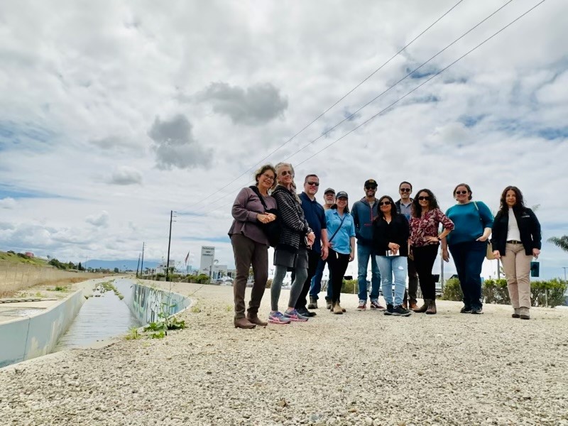 A group photo of men and women, standing along the side of the moon ditch drainage channel, with a partly cloudy sky in the background.